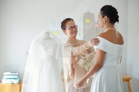 Téléchargez les photos : Mère heureuse regardant fille portant élégante robe de mariée blanche - en image libre de droit
