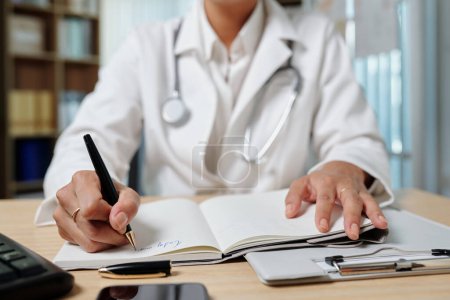 Téléchargez les photos : Image recadrée du médecin généraliste remplissant le planificateur lorsque vous travaillez au bureau médical - en image libre de droit