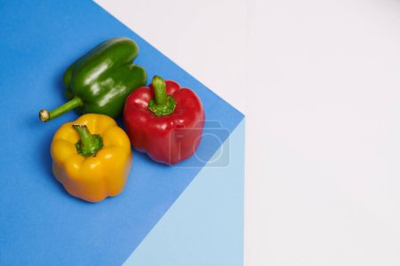 Téléchargez les photos : Poivrons rouges, jaunes et verts sur table bleue, concept de mode de vie sain - en image libre de droit