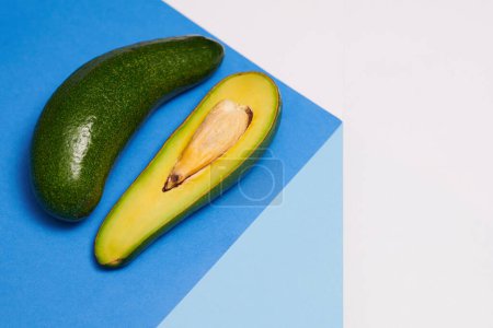Photo for Long avocado and a half on blue table, healthy eating concept - Royalty Free Image