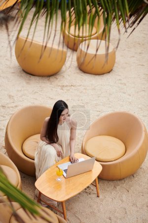Photo for Young woman working on laptop on beach of luxurious spa hotel - Royalty Free Image