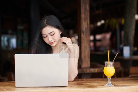 Téléchargez les photos : Jeune femme boire un cocktail de jus et de travailler sur ordinateur portable au bar de la plage - en image libre de droit