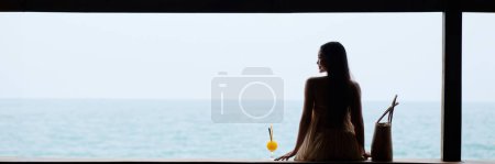 Photo for Young woman in flowing dress enjoying beautiful seascape and drinking fruit cocktail - Royalty Free Image