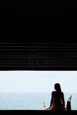 Photo for Header with smiling woman in flowing dress sitting next to glass of cocktail and enjoying beautiful seascape - Royalty Free Image