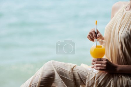 Photo for Cropped image of young woman in silk dress drinking orange juice - Royalty Free Image