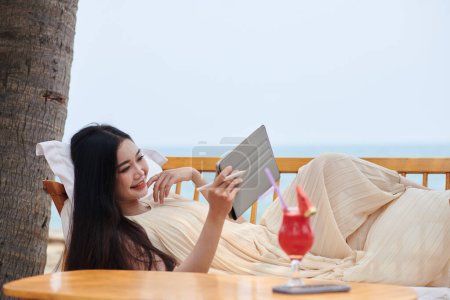 Photo for Happy young woman relaxing on patio sofa and watching entertaining videos on tablet computer - Royalty Free Image