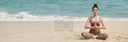 Téléchargez les photos : En-tête avec jeune femme méditant en position lotus sur une plage de sable fin - en image libre de droit