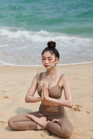 Téléchargez les photos : Jeune femme asiatique profitant de la méditation matinale sur la plage ensoleillée de la mer - en image libre de droit