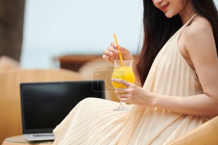 Téléchargez les photos : Image recadrée d'une jeune femme buvant un cocktail de fruits lors de la détente sur la plage après le travail - en image libre de droit