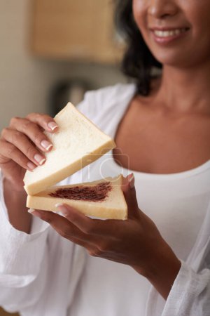 Photo for Young woman makingsandwich with two slices of bread and berry jam - Royalty Free Image