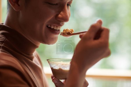 Photo for Cropped image of smiling young man eating bowl of oatmeal for breakfast - Royalty Free Image