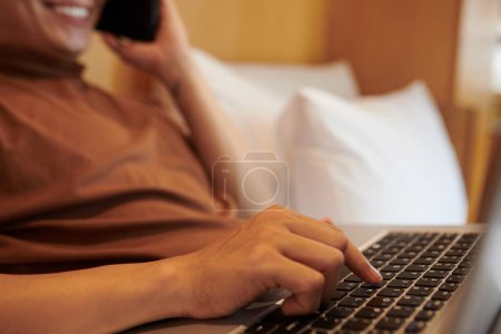 Téléchargez les photos : Jeune homme appuyant sur le bouton sur un ordinateur portable lorsque vous parlez au téléphone avec un collègue ou un client - en image libre de droit