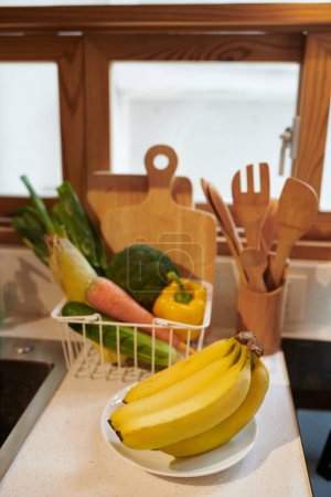 Téléchargez les photos : Bunch de bananes fraîches et panier en métal de comptoir de cuisine de légumes - en image libre de droit