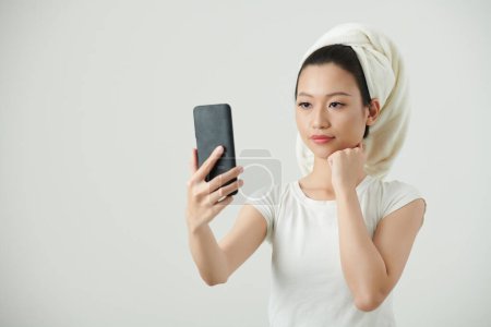 Photo for Young Vietnamese woman taking selfie on smartphone after shower - Royalty Free Image
