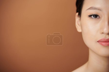 Téléchargez les photos : Demi-visage de jeune femme asiatique avec doublure des yeux et teinte des lèvres regardant la caméra - en image libre de droit