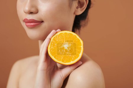 Téléchargez les photos : Image recadrée d'une jeune femme tenant un concept d'orange coupée, d'huiles essentielles et de cosmétiques bio - en image libre de droit