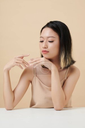 Téléchargez les photos : Pensive jeune femme assise à table et jouissant de la beauté de ses doigts - en image libre de droit