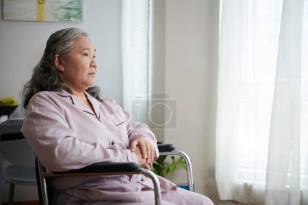 Photo for Lonely senior woman with disability sitting in wheelchair in nursing home bedroom - Royalty Free Image
