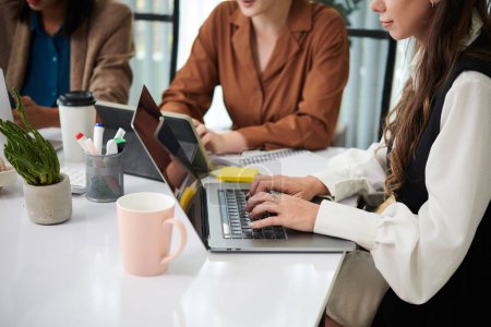 Téléchargez les photos : Image recadrée de femmes d'affaires travaillant sur des ordinateurs portables à la table de bureau - en image libre de droit
