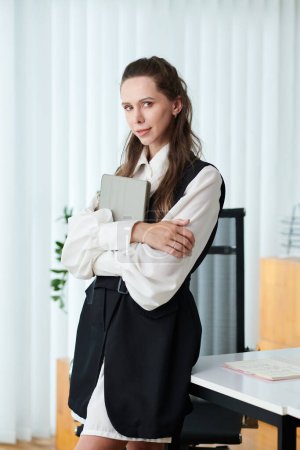 Foto de Mujer de negocios exitosa con tableta digital de pie en el escritorio de la oficina y mirando a la cámara - Imagen libre de derechos