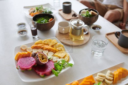 Téléchargez les photos : Assiette avec des fruits frais coupés, théière et bols de soupe de table de café - en image libre de droit