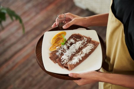 Téléchargez les photos : Serveur apportant des crêpes au chocolat avec des tranches de banane et des flocons de noix de coco à la table de café - en image libre de droit