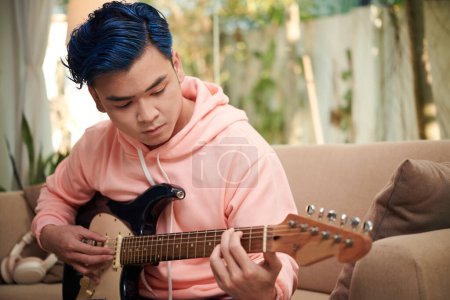 Foto de Concentrado creativo joven con pelo azul tocando la guitarra ta casa - Imagen libre de derechos