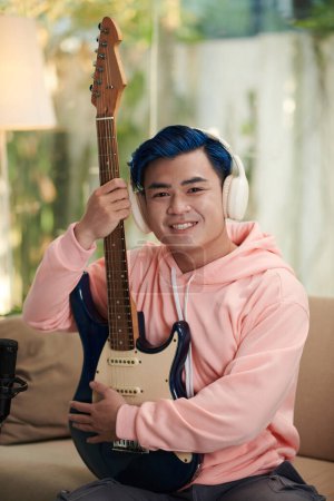 Téléchargez les photos : Portrait de musicien heureux dans les écouteurs posant avec guitare électrique - en image libre de droit