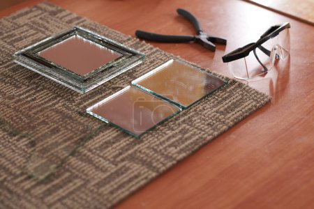 Foto de Pequeñas piezas de espejo cortadas, alicates y gafas en la mesa en el taller - Imagen libre de derechos