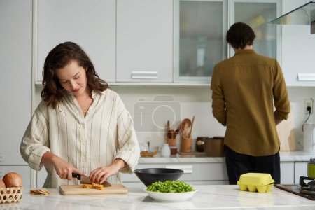 Foto de Mujer joven cortando calabazas en trozos pequeños cuando novio cocinar caldo para la sopa - Imagen libre de derechos