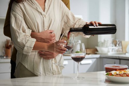 Photo for Cropped image of man hugging girlfriend when she is pouring red wine in glasses - Royalty Free Image