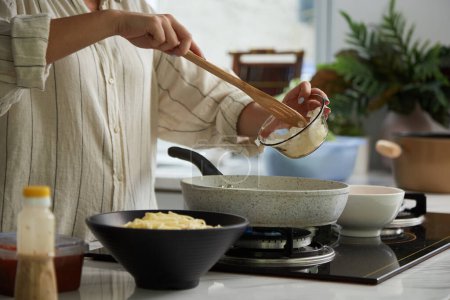 Téléchargez les photos : Image recadrée de la femme mettant l'oignon coupé en dés dans une casserole chaude - en image libre de droit