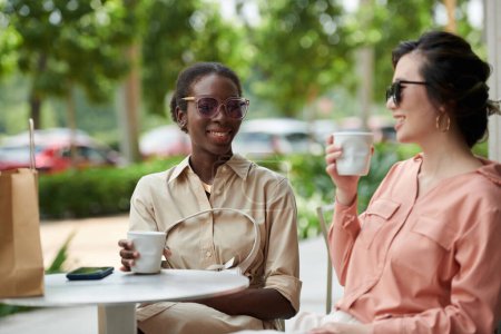 Photo for Smiling women drinking coffee and discussing sales and deals after shopping together - Royalty Free Image