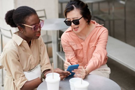 Foto de Mujer mostrando nueva tienda en línea a un amigo cuando están sentados en la mesa de café al aire libre - Imagen libre de derechos