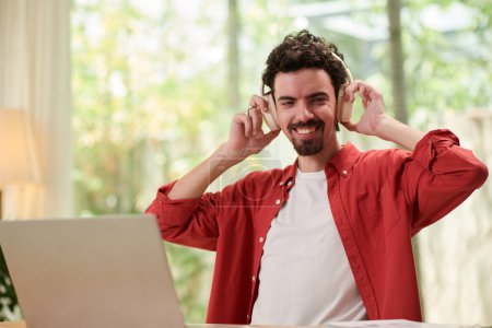 Photo for Portrait of joyful man listening to podcast or audiobook when working on laptop - Royalty Free Image