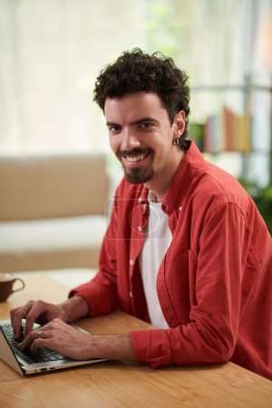 Photo for Portrait of smiling software developer working on laptop at desk in home office - Royalty Free Image
