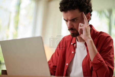Photo for Pensive frowning man reading programming code on laptop screen - Royalty Free Image