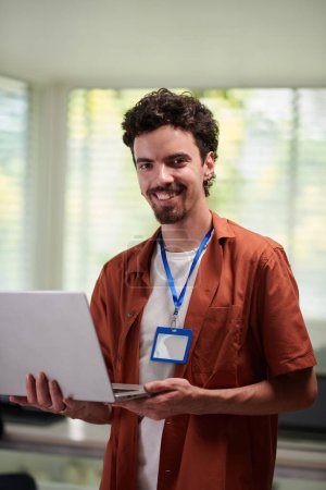 Téléchargez les photos : Portrait de programmeur heureux debout dans le bureau avec ordinateur portable ouvert - en image libre de droit
