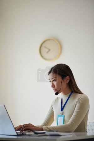 Téléchargez les photos : Femme d'affaires portant casque lorsque vous travaillez sur un ordinateur portable dans un bureau moderne - en image libre de droit