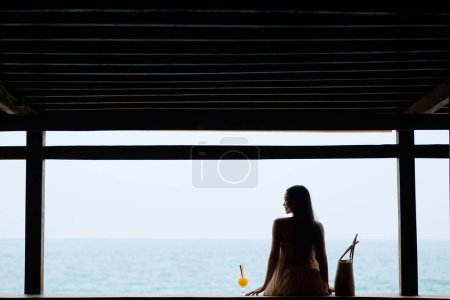 Photo for Young woman sitting next to glass of fruit juice and enjoying beautiful seascape - Royalty Free Image