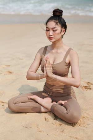 Foto de Mujer joven cogida de la mano en namaste mudra al meditar en la playa - Imagen libre de derechos