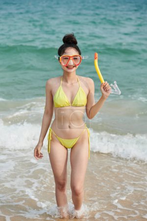 Foto de Mujer joven sonriente en bikini de pie en la playa de arena con máscara para el snorkel - Imagen libre de derechos