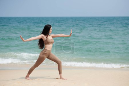 Téléchargez les photos : Fit jeune femme pratiquant le yoga sur la plage de sable fin - en image libre de droit