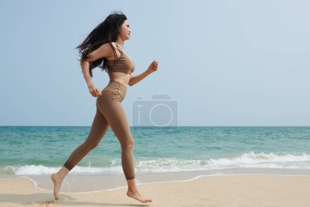 Téléchargez les photos : Fit jeune femme jogging sur la plage le matin - en image libre de droit