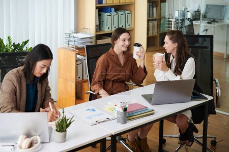 Foto de Grupo de colegas hablando entre sí y tomando café en la mesa durante el descanso en la oficina - Imagen libre de derechos