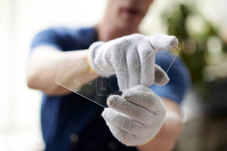 Foto de Vidriero con guantes mostrando vidrio cortado a la cámara durante su trabajo en el taller - Imagen libre de derechos