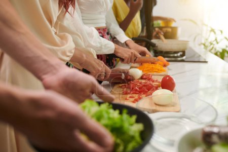 Foto de Manos de gente cortando verduras al cocinar comida en clase culinaria - Imagen libre de derechos