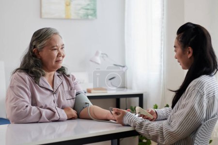 Foto de Cuidador del hogar de ancianos que mide la presión arterial de la mujer mayor - Imagen libre de derechos