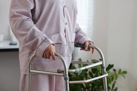 Téléchargez les photos : Image recadrée de femme âgée se déplaçant autour de la maison avec marcheur - en image libre de droit