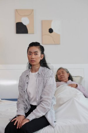 Téléchargez les photos : Portrait d'une jeune femme triste et inquiète assise sur le lit de sa mère malade - en image libre de droit